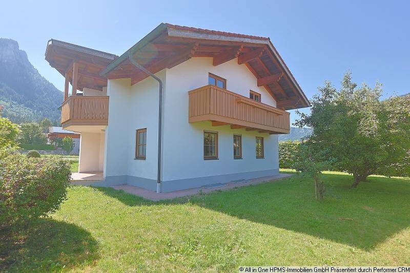 Rückansicht des Hauses mit Holzbalkon, weißer Fassade und Blick auf die umliegende Berglandschaft.