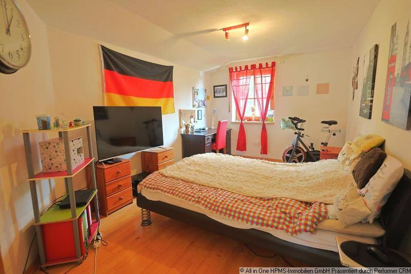 Jugendliches Schlafzimmer mit Bett, Schreibtisch, Sportgerät und farbigen Vorhängen am Fenster.