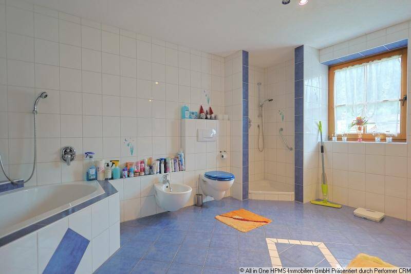 Geräumiges Badezimmer mit blauen und weißen Fliesen, Badewanne, Dusche, WC und Fenster für Tageslicht.