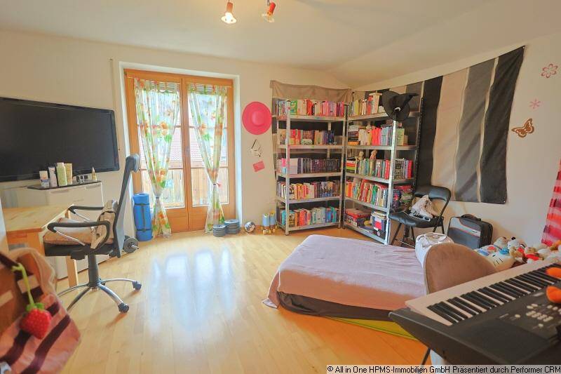 Helles Schlafzimmer mit Holzboden, Bücherregalen, Fernseher und direktem Zugang zu einem Balkon.