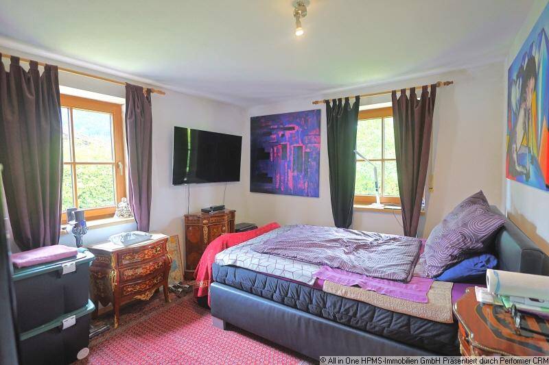 Gemütliches Schlafzimmer mit Doppelbett, Fernseher und zwei Fenstern, die viel Tageslicht hereinlassen.