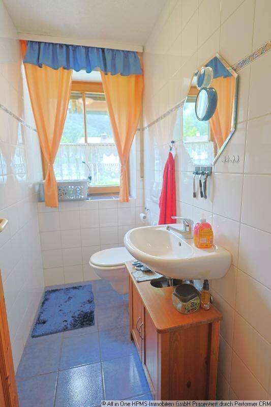 Kleines Gäste-WC mit Fenster, Waschbecken und Toilette, ausgestattet mit hellen Fliesen und bunten Vorhängen.