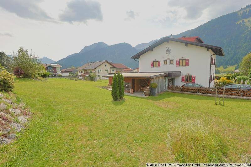 Traditionelles Haus mit rotem Dach und großem Garten, umgeben von einer malerischen Berglandschaft.
