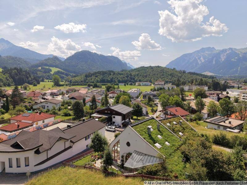 Panoramablick auf eine malerische Stadt im Tal, umgeben von majestätischen Bergen und grünen Dächern.