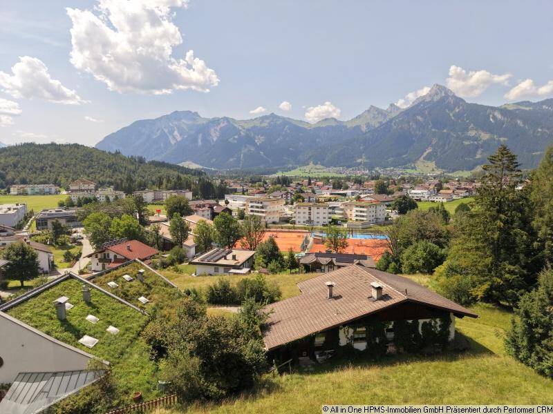 Weitläufiger Ausblick auf die Stadt und die umliegende Berglandschaft mit einem Tennisplatz im Vordergrund.