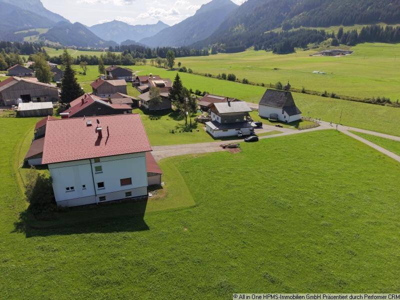 Weitläufige Ansicht des Wohnhauses in einem ländlichen Dorf mit umliegenden Wiesen und Bergen.