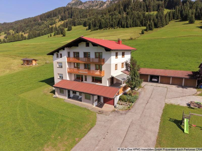 Wohnhaus in alpiner Landschaft mit mehreren Balkonen und angrenzender Garage, umgeben von Natur.