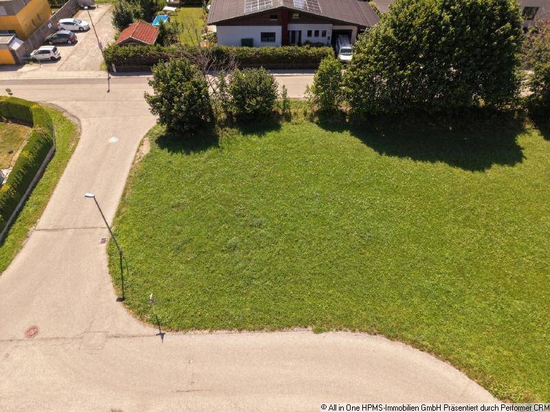Luftaufnahme eines unbebauten Grundstücks an einer Straßenecke, umgeben von Wohnhäusern und Bäumen.