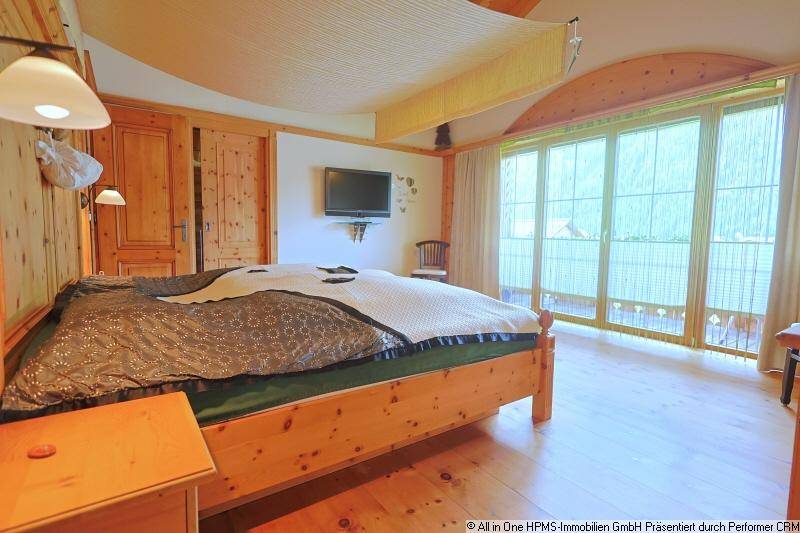 Helles Schlafzimmer mit Holzbett, Holzboden und Zugang zu einem Balkon mit Bergblick.