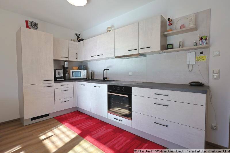 Moderne Einbauküche mit hellen Schränken, dunkler Arbeitsplatte und integrierten Geräten.
