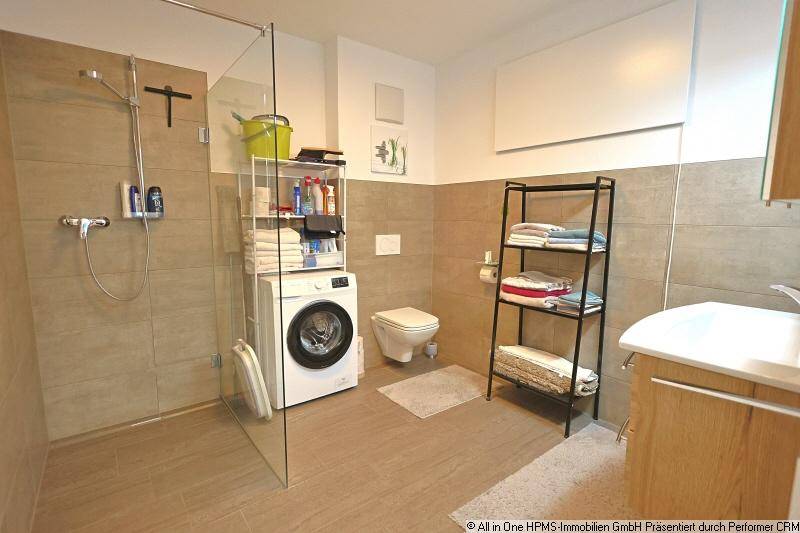 Modernes Badezimmer mit ebenerdiger Dusche, WC, Waschbecken und Waschmaschine.