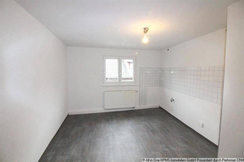 Leere Küche mit grauem Boden, Fenster und gefliestem Wandbereich, bereit für Einbauküche.