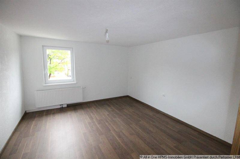 Geräumiger, leerer Raum mit Laminatboden und Fenster, ideal als Schlaf- oder Kinderzimmer.