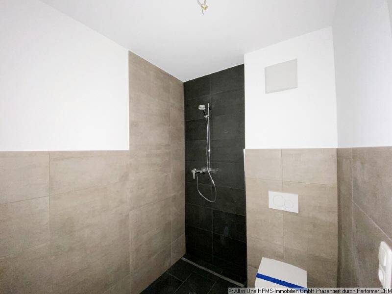 Modernes Badezimmer mit ebenerdiger Dusche und wandhängender Toilette in hellen und dunklen Fliesen.