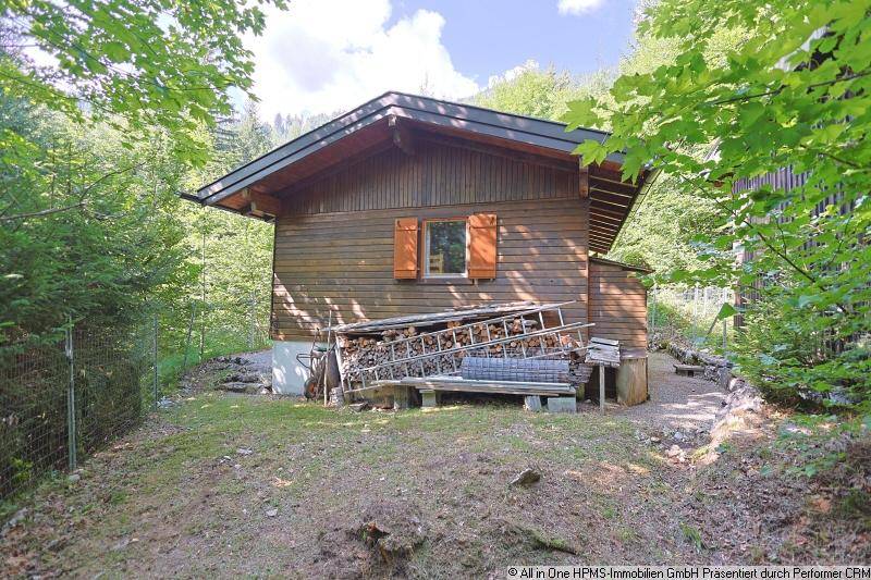 Seitenansicht der Holzhütte mit einem Stapel Brennholz und umgeben von Wald.