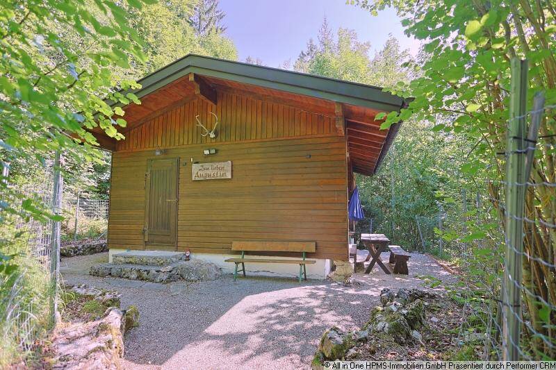 Vorderansicht der Holzhütte mit rustikalen Sitzgelegenheiten im Freien und Waldkulisse.