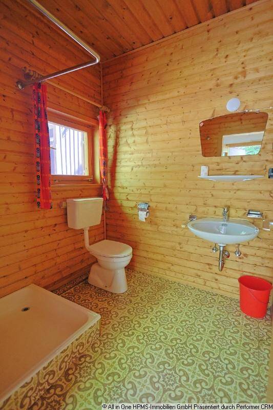 Badezimmer mit Holzvertäfelung, WC, Waschbecken und einem Fenster für Tageslicht.