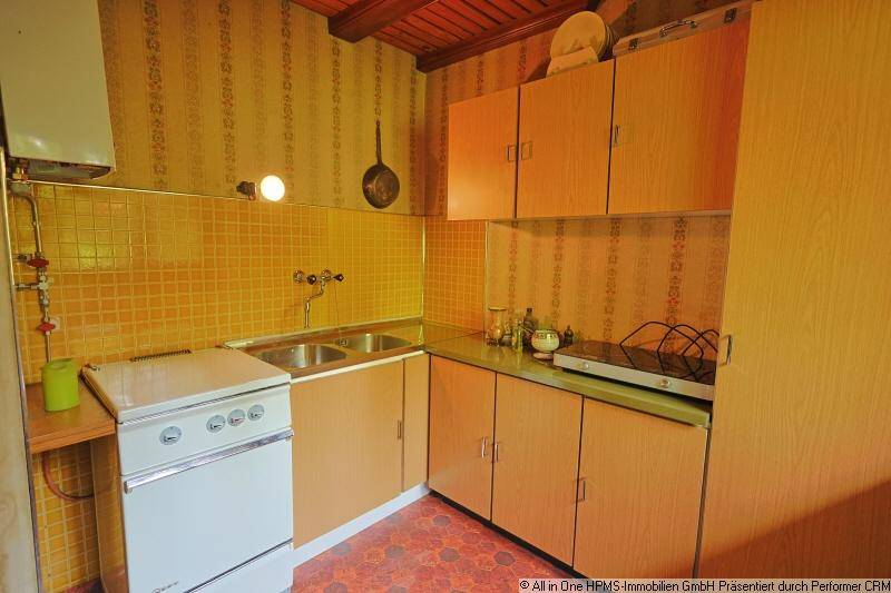Funktionale Küche mit gelben Wandfliesen, älteren Geräten und Holzschränken.