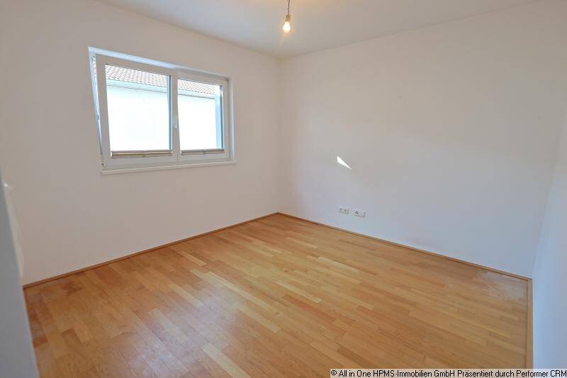 Helles Schlafzimmer mit Holzparkettboden und einem Fenster, das viel Tageslicht hereinlässt.