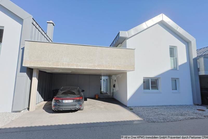 Vorderansicht eines modernen Hauses mit weißer Fassade und integriertem Carport für ein Fahrzeug.