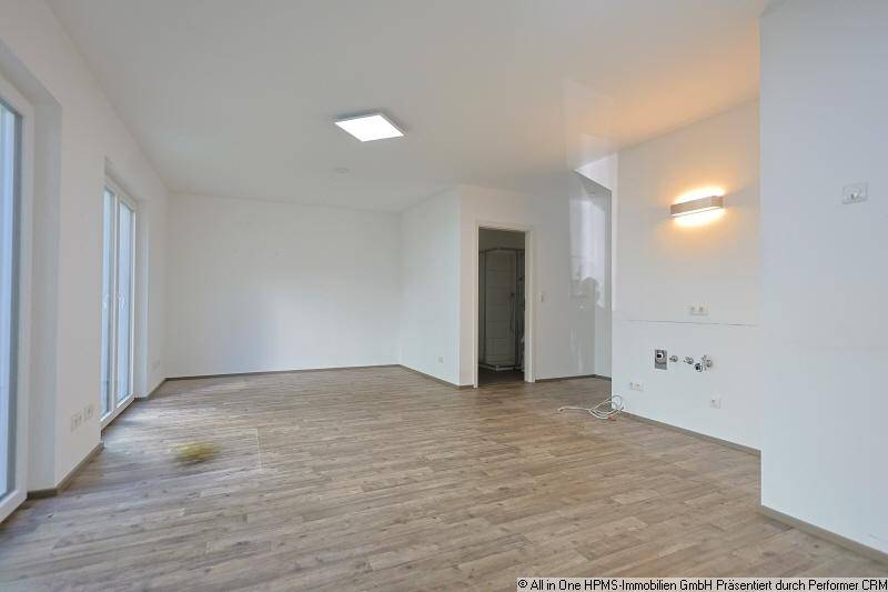 Geräumiger, heller Raum mit Holzoptikboden und großen Fenstern, ideal als Wohnzimmer.