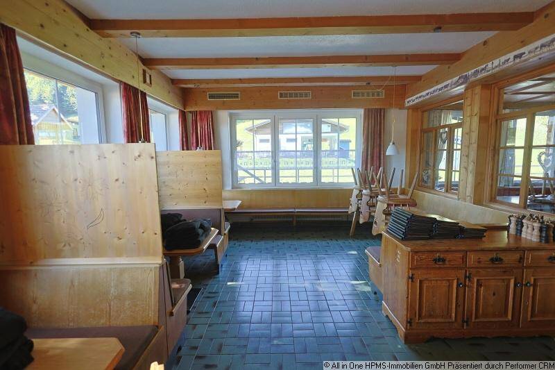 Rustikaler Essbereich mit Holzbänken, gefliestem Boden und Fenstern mit Blick nach draußen.