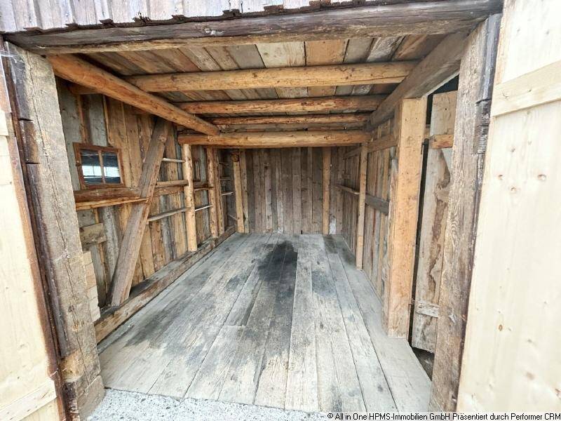 Rustikaler Innenraum einer Holzscheune mit sichtbaren Holzbalken und Dielenboden.