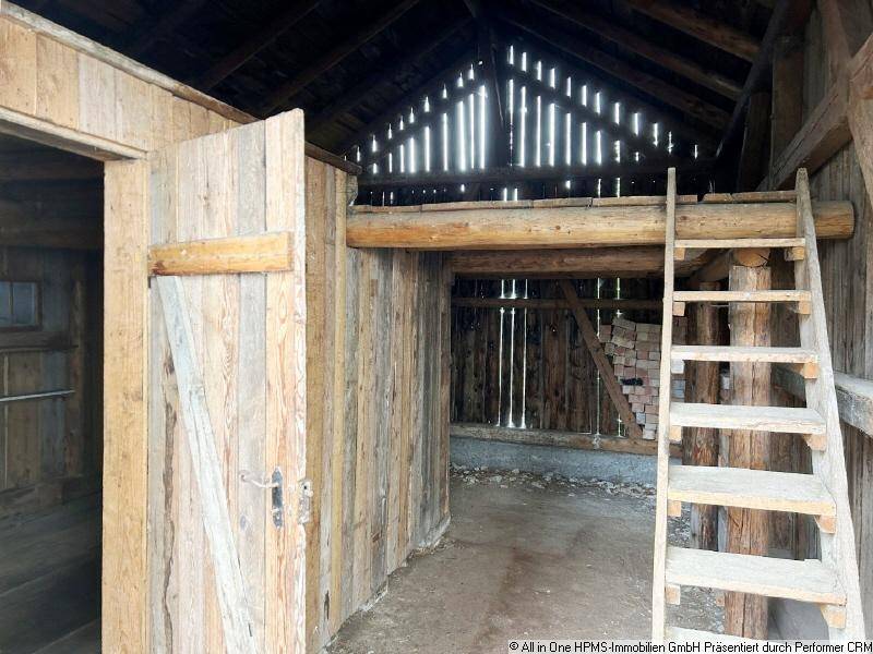 Innenansicht einer Holzscheune mit Leiter zum oberen Bereich und sichtbaren Holzbalken.