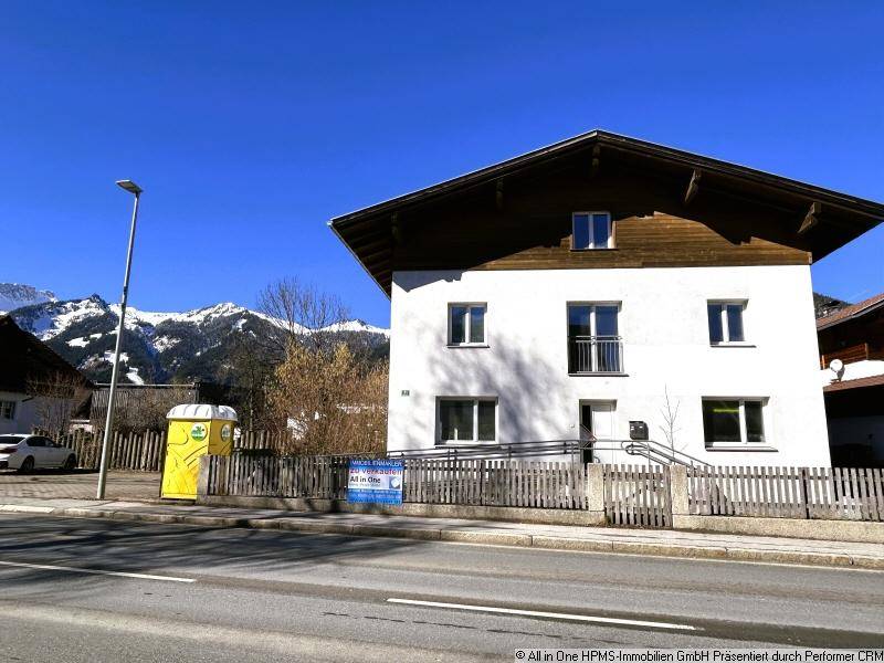 Weißes Wohnhaus mit traditionellem Dach und Rampe am Eingangsbereich, umgeben von Bergen.