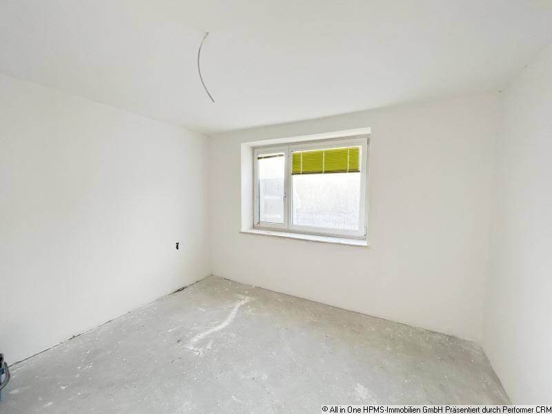 Leerer Raum mit weißen Wänden, einem Fenster und Betonboden, bereit für den Ausbau.