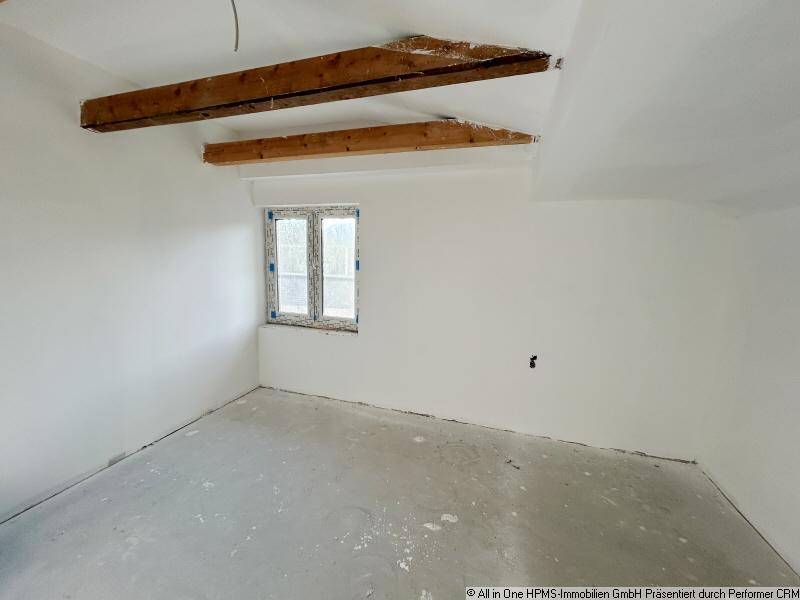 Unmöblierter Raum mit sichtbaren Holzbalken, weiß gestrichenen Wänden und Fenster.