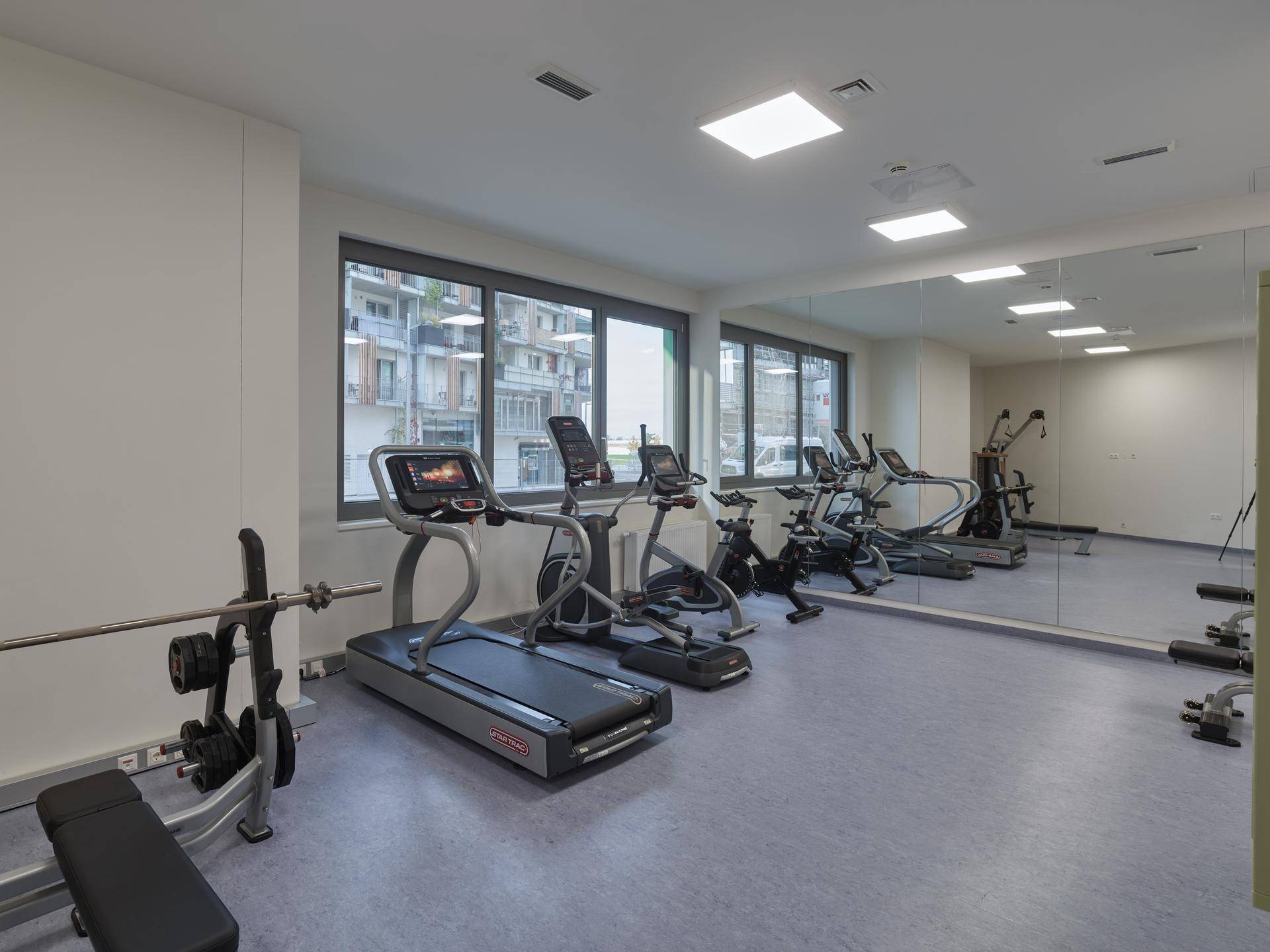 Gut ausgestatteter Fitnessraum mit verschiedenen Trainingsgeräten und großen Fenstern.