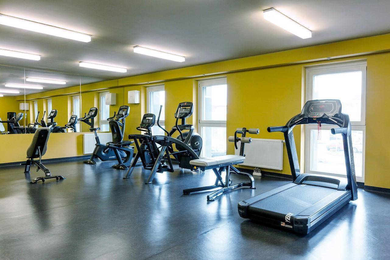 Gut ausgestatteter Fitnessraum mit verschiedenen Trainingsgeräten und großen Spiegelflächen.