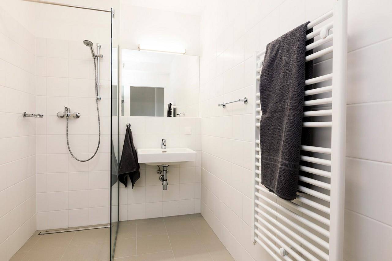 Modernes Badezimmer mit ebenerdiger Dusche, weiß gefliesten Wänden und beheiztem Handtuchhalter.