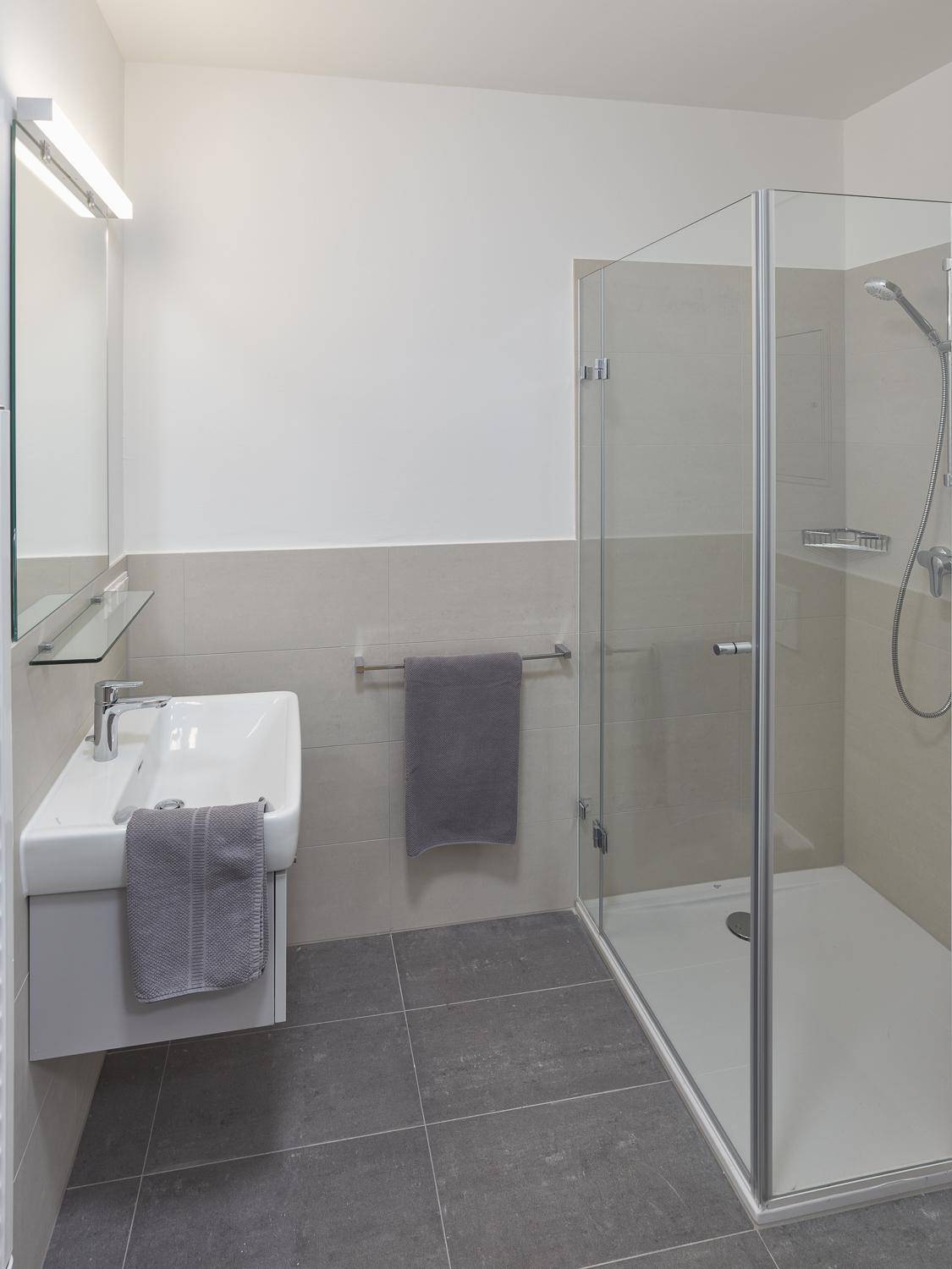 Modernes Badezimmer mit begehbarer Dusche, Wandwaschbecken und hellen Fliesen.