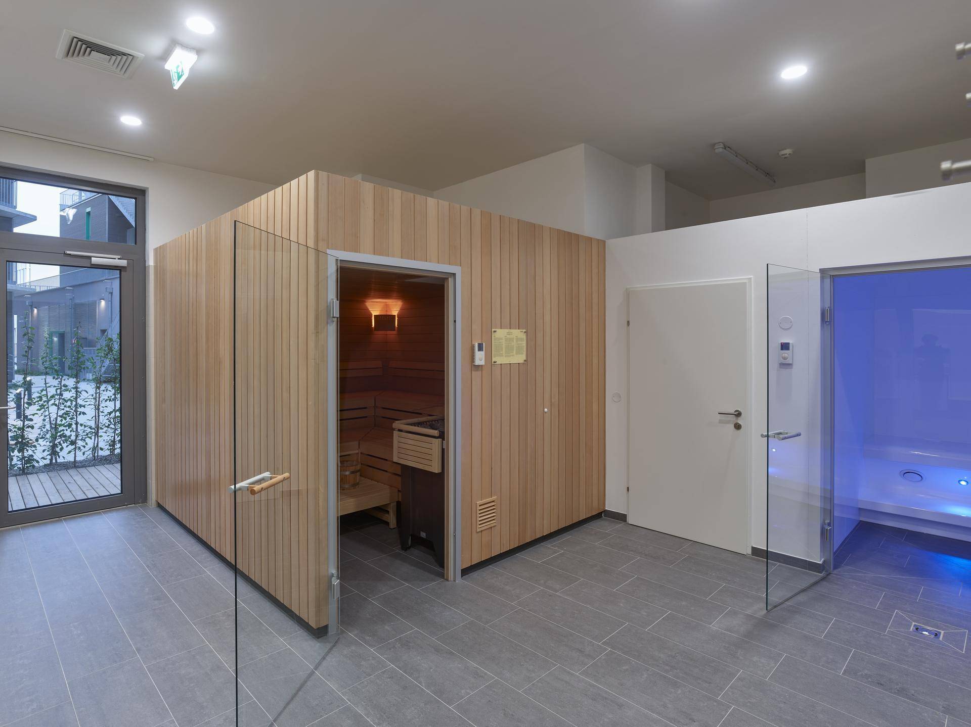 Moderner Wellnessbereich mit Sauna, Whirlpool und Zugang zu einem Außenbereich.