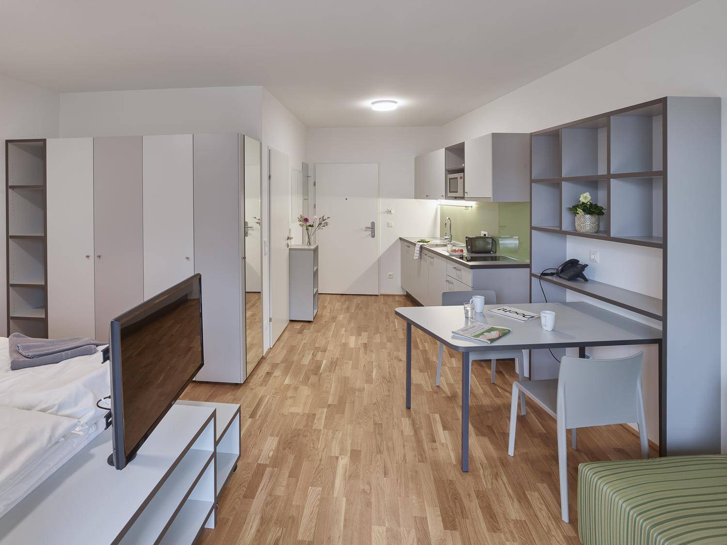 Heller Wohnbereich mit Küchenzeile, Esstisch und Schränken, ideal für ein Studio-Apartment.