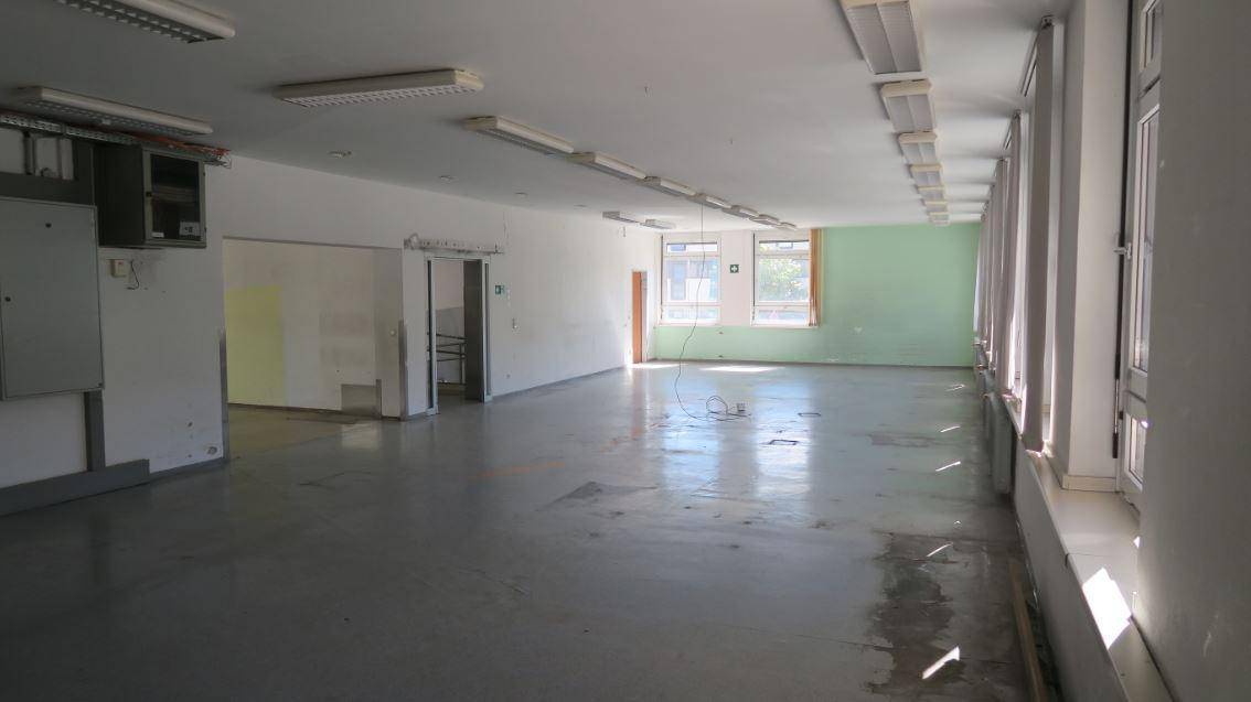Großer, leerer Raum mit mehreren Fenstern und Leuchtstoffröhren an der Decke, bereit zur Renovierung.