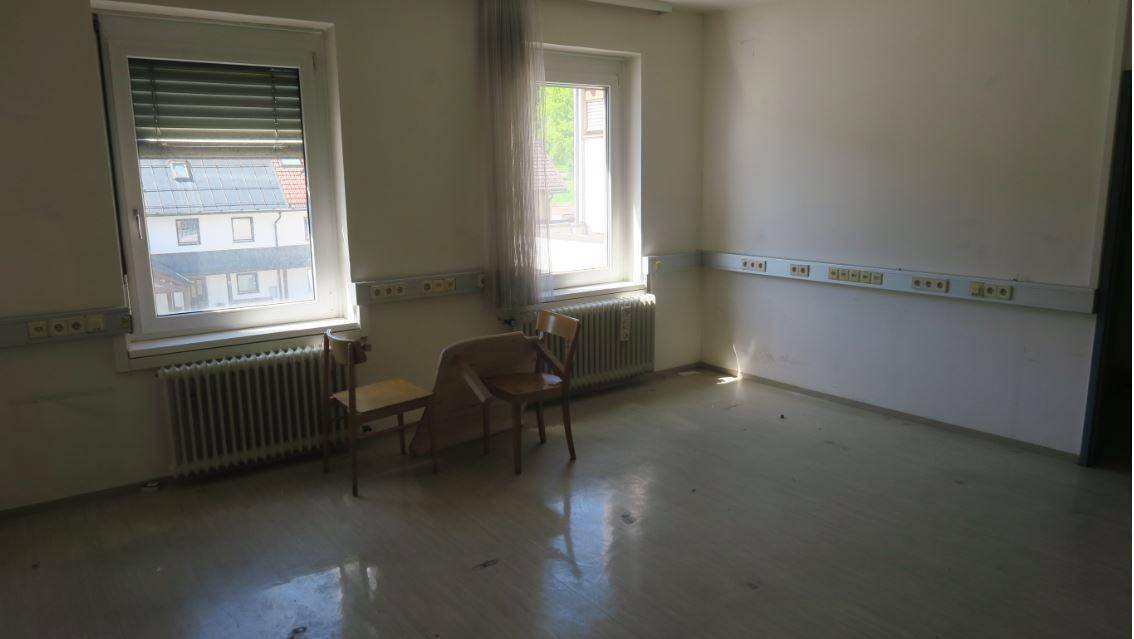 Heller Raum mit zwei Fenstern, Heizkörpern und einfacher Ausstattung, ideal für ein Büro.