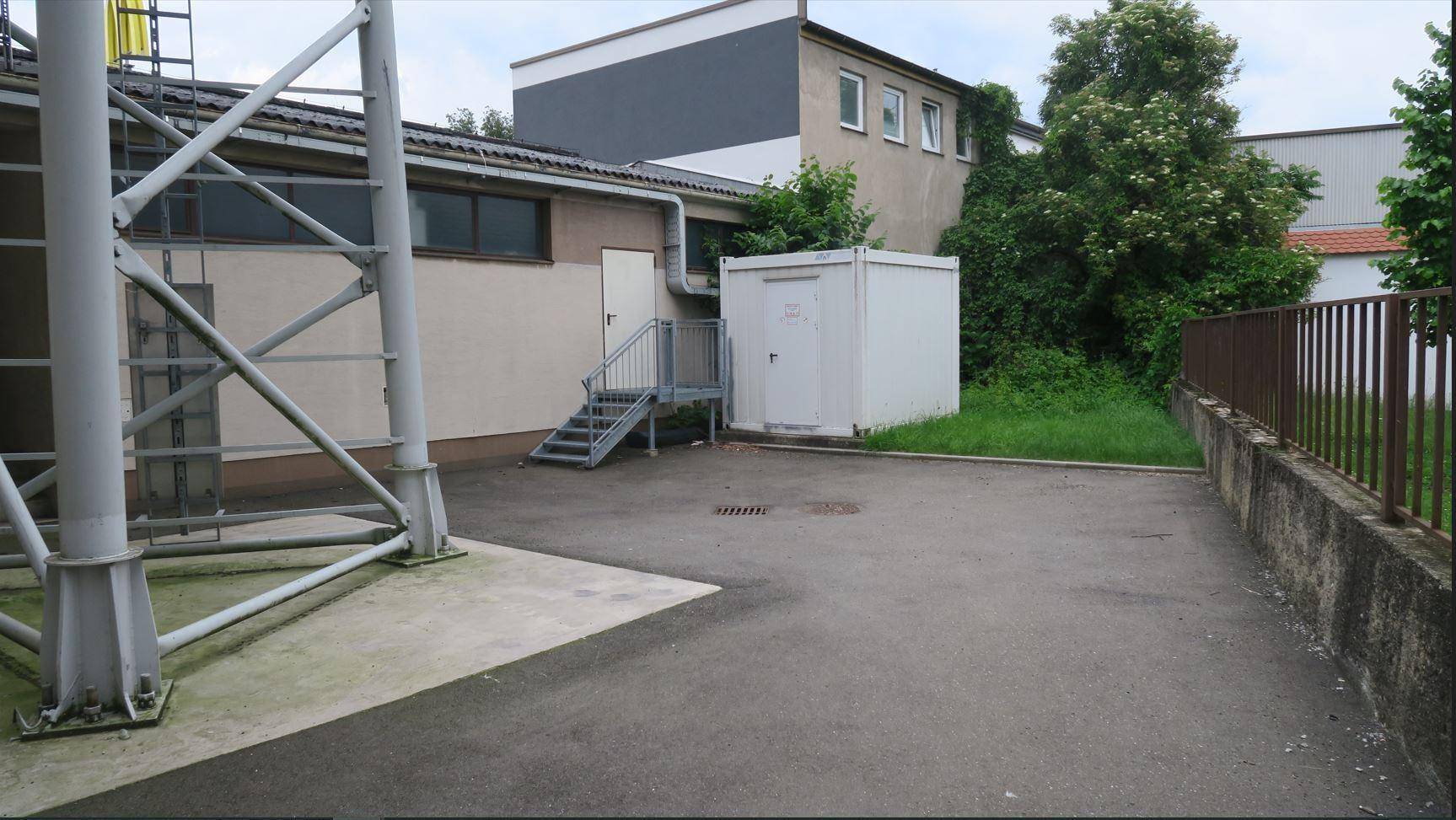 Hinterhofbereich mit Asphaltfläche, einem Container und Treppenaufgang zu einem Nebengebäude.