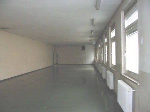 Langer, leerer Raum mit vielen Fenstern und Heizkörpern entlang einer Wand, bereit zur Renovierung.