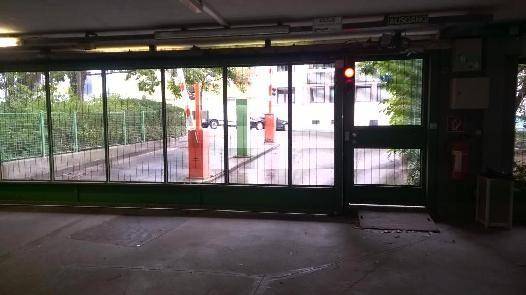 Blick aus der Tiefgarage durch eine Glasfront auf die Einfahrtsschranke und Bäume.