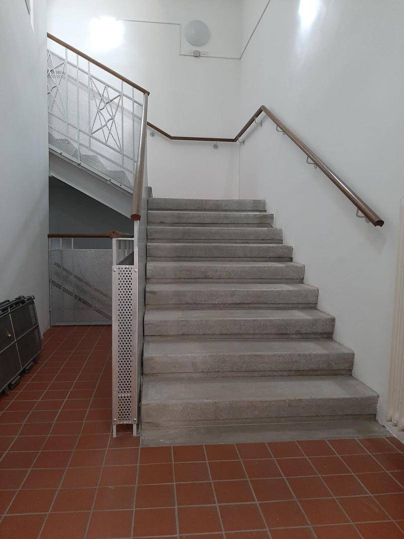 Treppenhaus mit Steinstufen, Metallgeländer und Terrakotta-Fliesenboden im Eingangsbereich.
