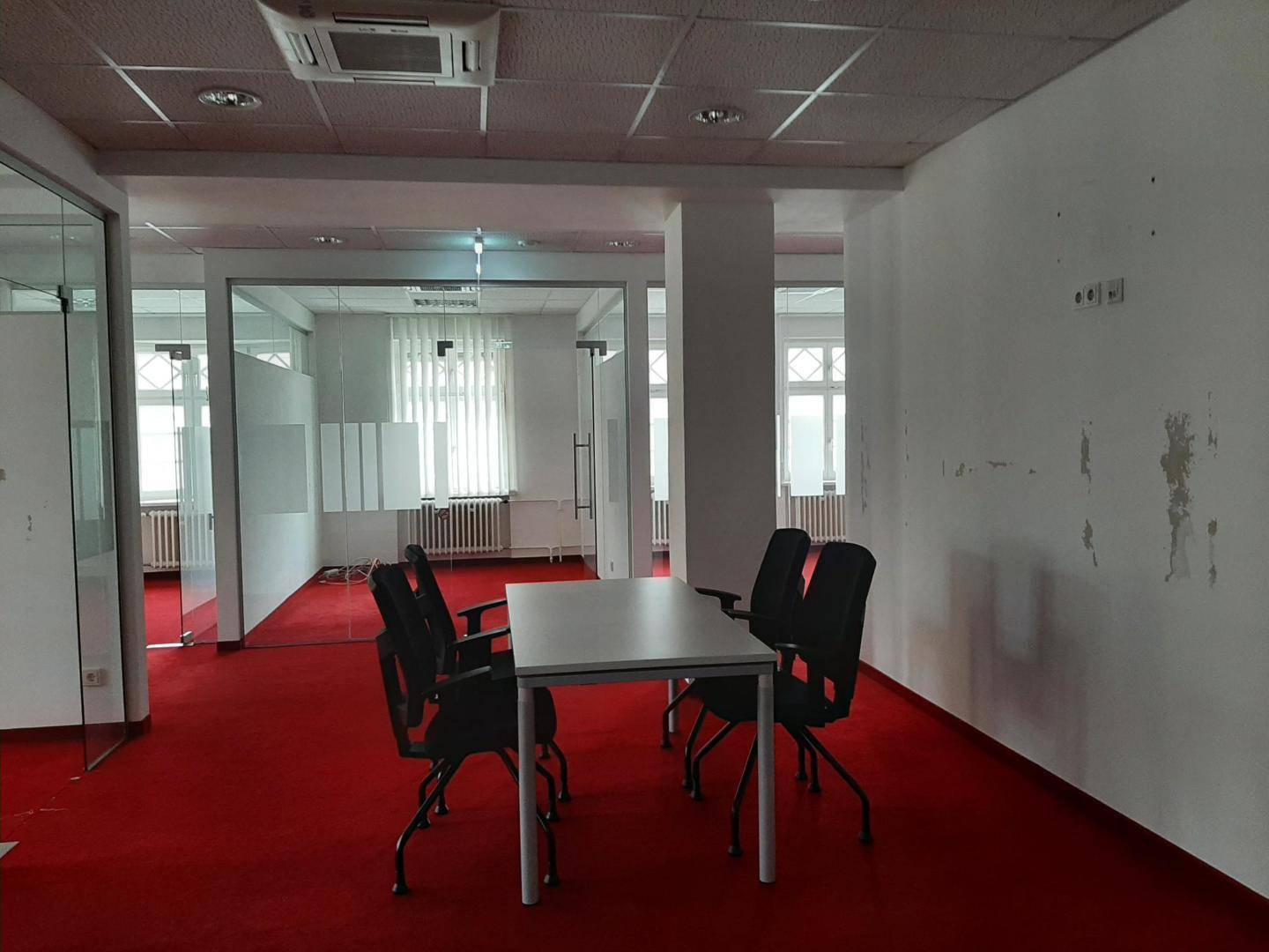 Bürobereich mit rotem Teppichboden, einem Besprechungstisch und Glaswänden zu angrenzenden Räumen.