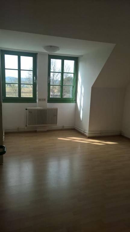 Ein leerer Raum mit Laminatboden, zwei großen Fenstern und einer Dachschräge, der viel Tageslicht erhält.