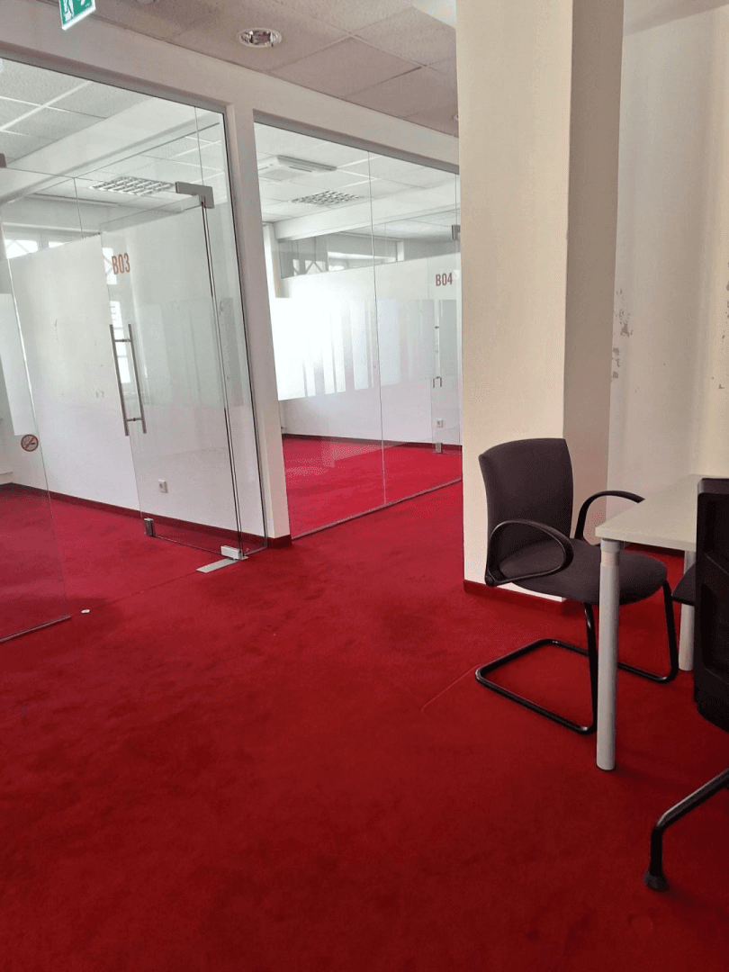Bürofläche mit rotem Teppichboden und Glasabtrennungen, die mehrere Arbeitsbereiche in einem hellen Raum schaffen.