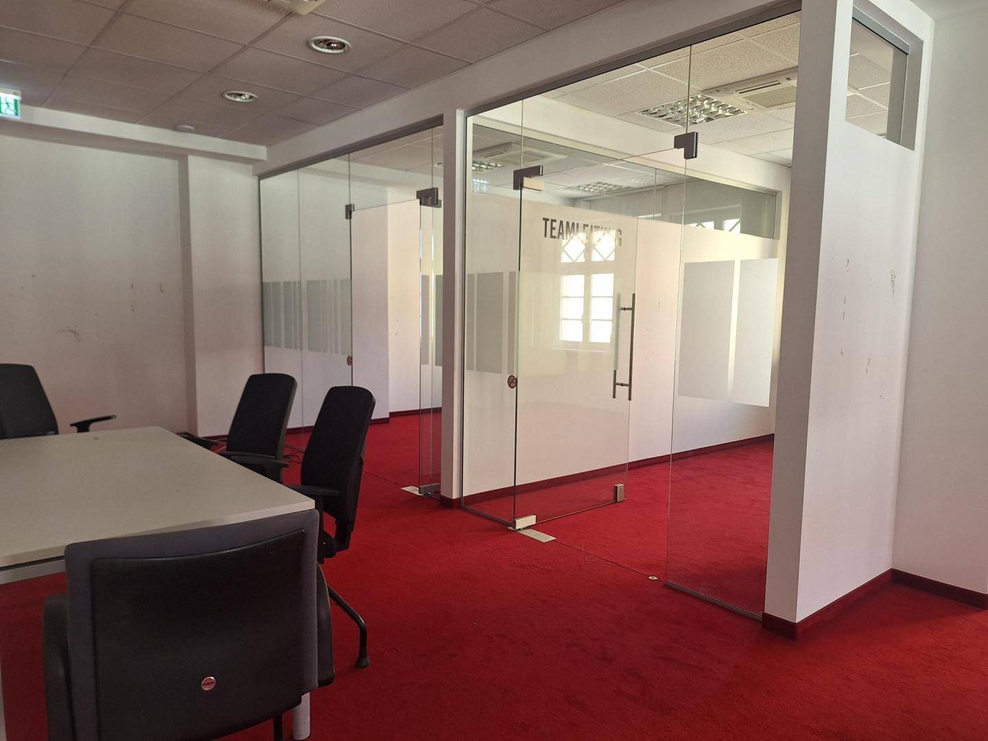 Modernes Büro mit leuchtend rotem Teppichboden und Glaswänden, die separate Arbeitsbereiche schaffen.