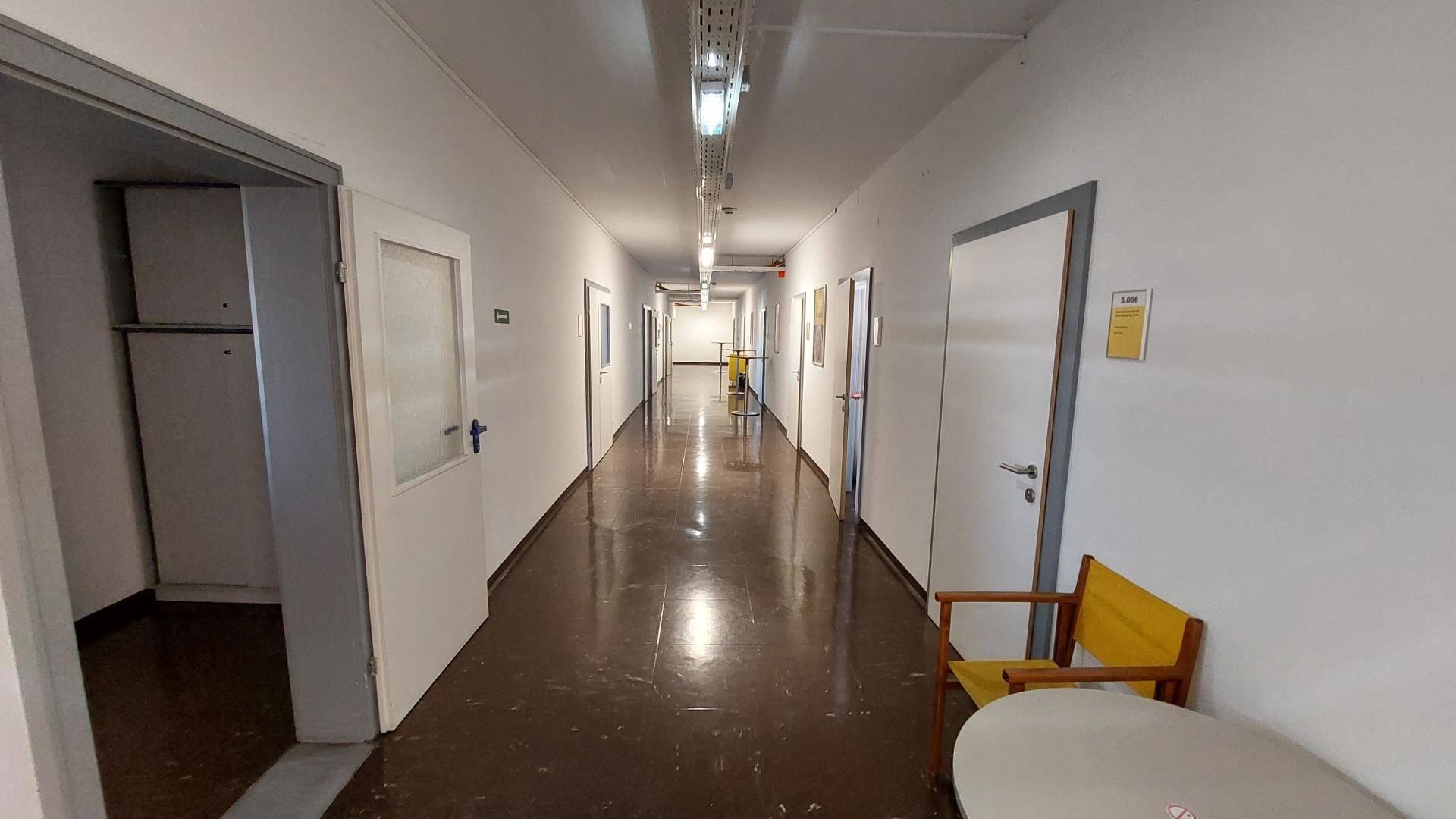 Langer, leerer Flur mit vielen Türen auf beiden Seiten und funktionaler Deckenbeleuchtung.