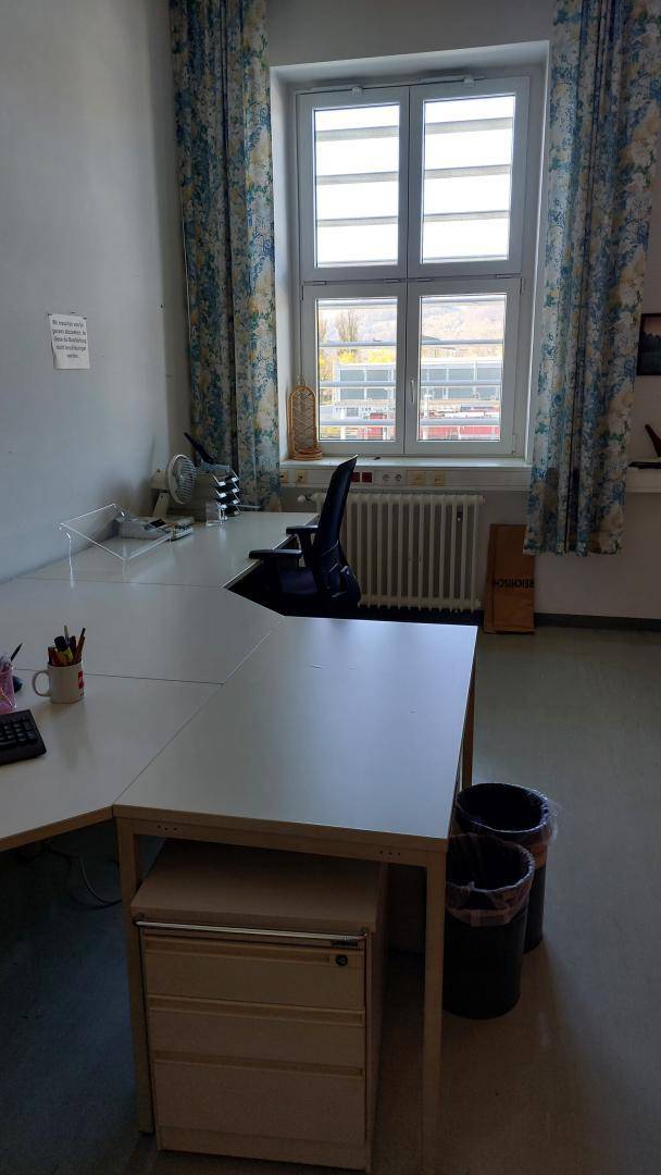 Helles Büro mit einem Schreibtisch, Bürostuhl und einem Fenster mit gemusterten Vorhängen.