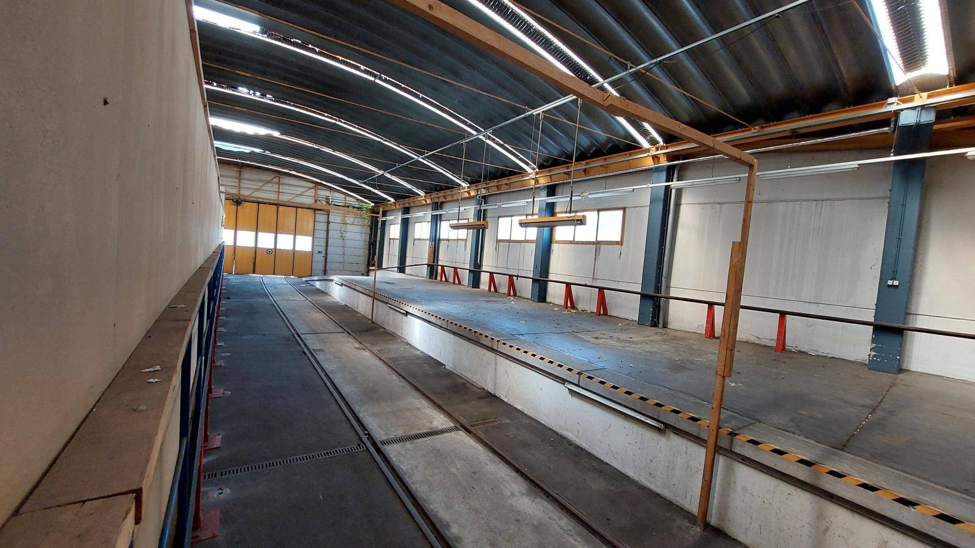 Innenansicht einer geräumigen Industriehalle mit gewölbtem Dach, Inspektionsgruben und einem großen Rolltor.